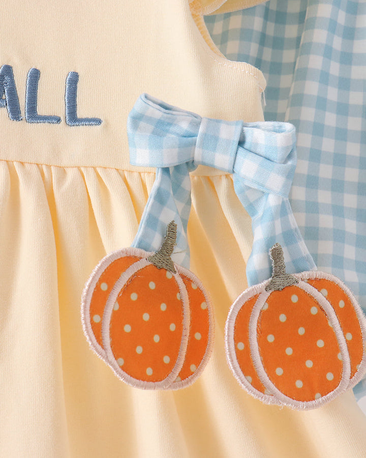 Close-up of a baby dress featuring orange pumpkin appliqués with white polka dots, a light blue gingham bow, and a light blue and white gingham fabric panel.