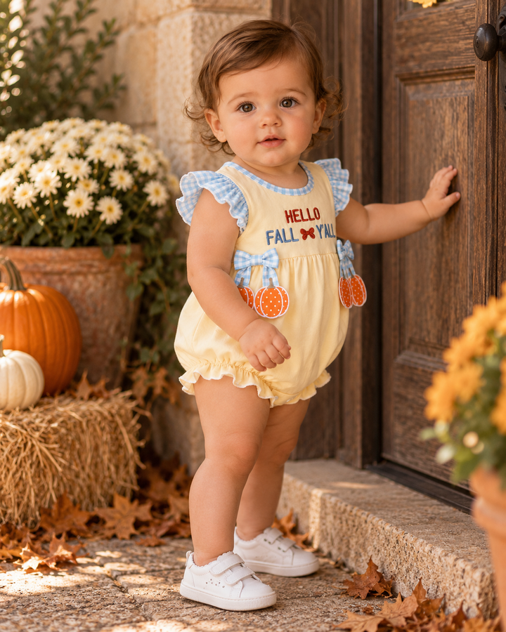 Baby girl in a pumpkin outfit is standing by a wooden front door.
