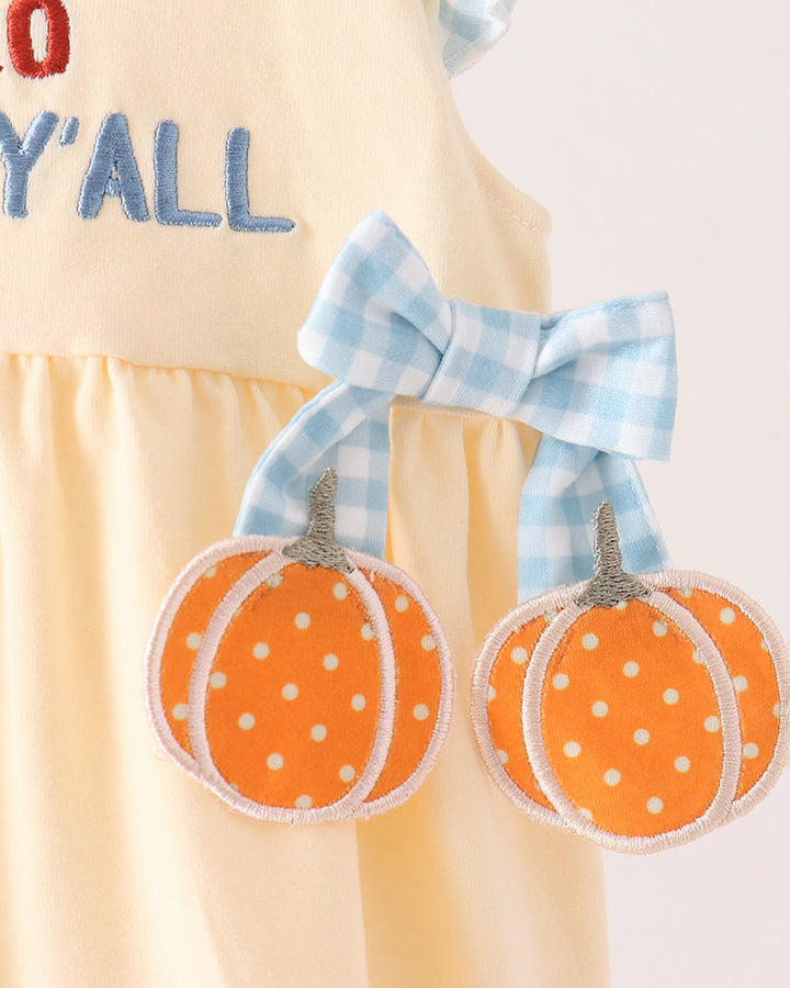 A close-up of a light yellow dress with blue gingham trim and applique, featuring embroidered text &