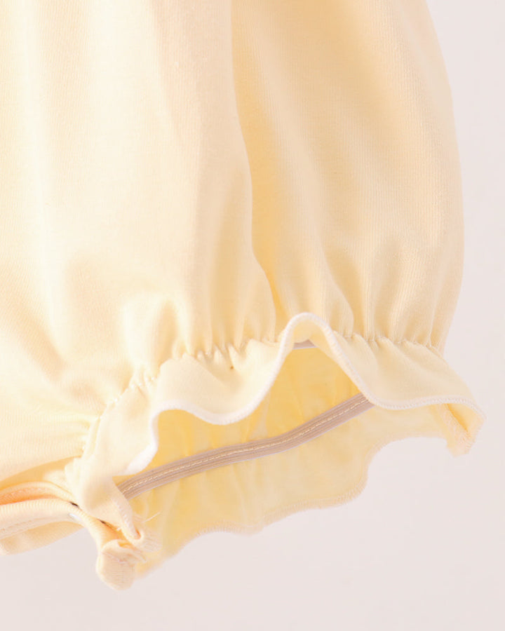 Close-up of a pale yellow fabric garment with a gathered elastic cuff and a thin light gray stripe detail, shown against a plain light background.