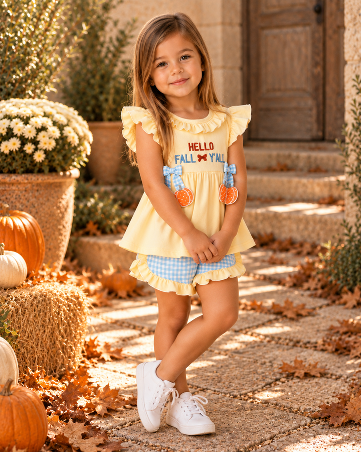 A young girl stands on a stone path outdoors wearing a pale yellow ruffle-sleeve top with &