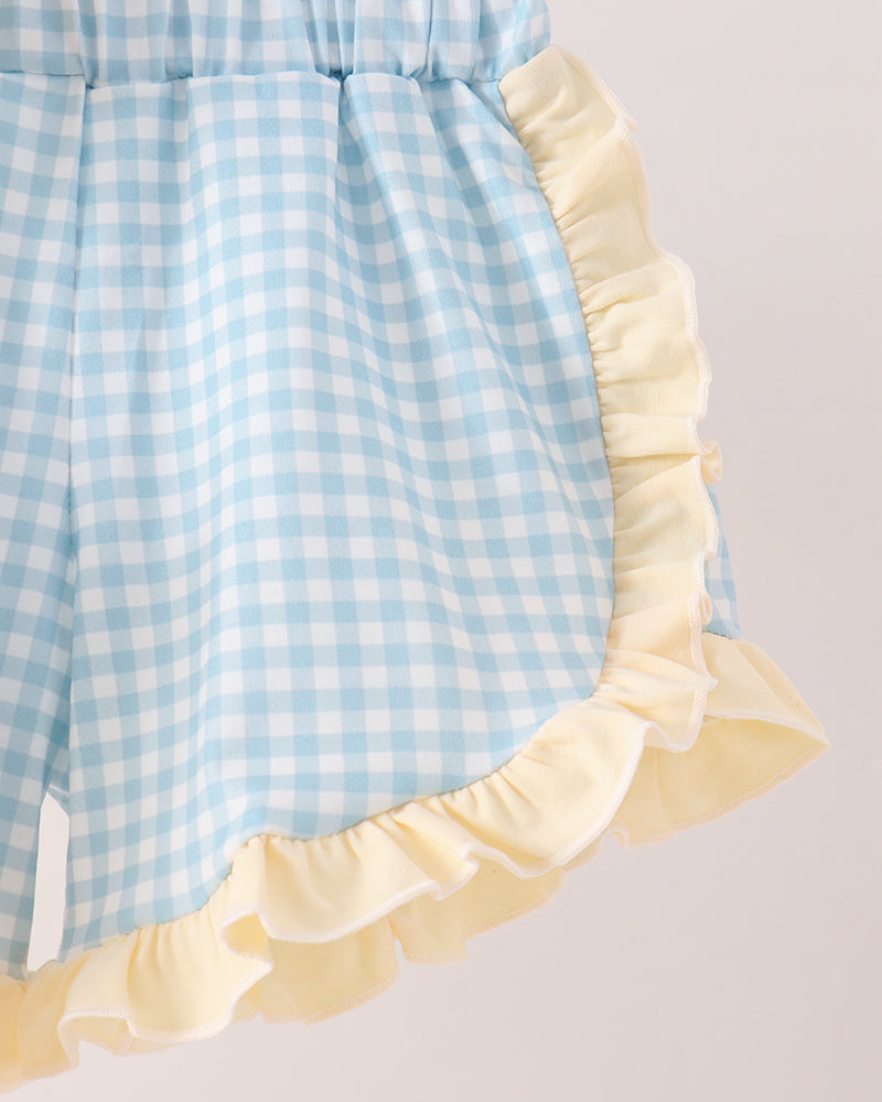 Close-up of a light blue and white gingham shorts with a pale yellow ruffled trim, shown against a plain light background.