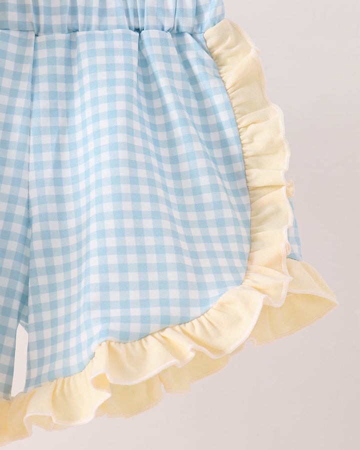 Close-up of a light blue and white gingham shorts with a pale yellow ruffled trim, shown against a plain light background.