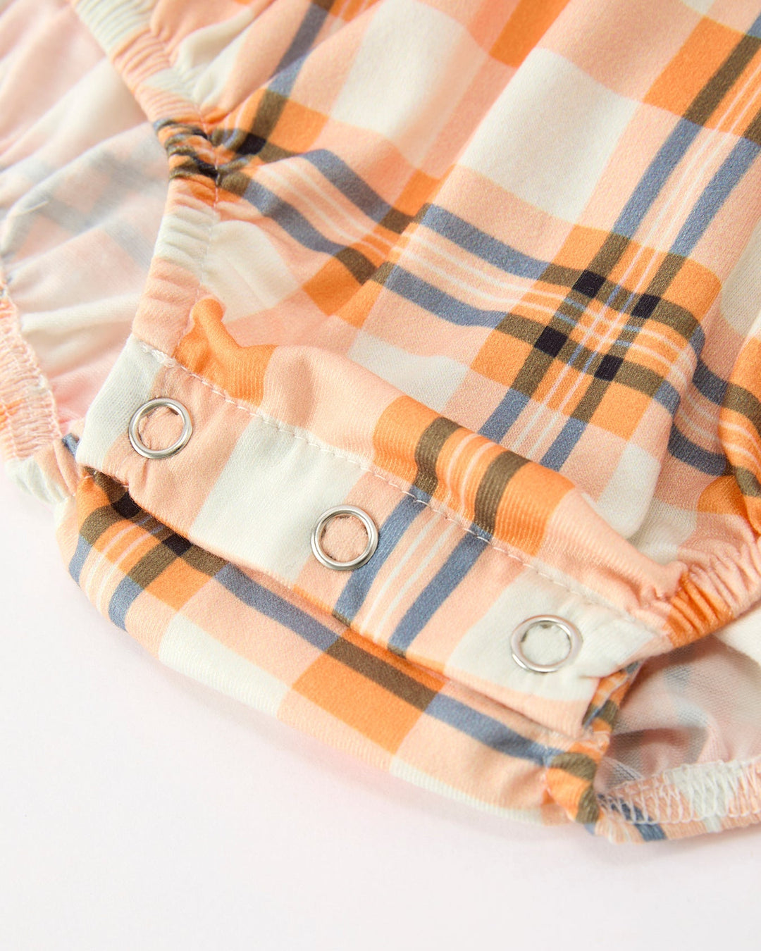 Orange plaid baby romper leg close-up with snap buttons and round eyelets