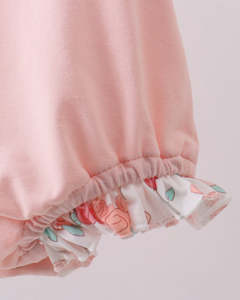 Close-up of a pink romper with floral hem on a light background