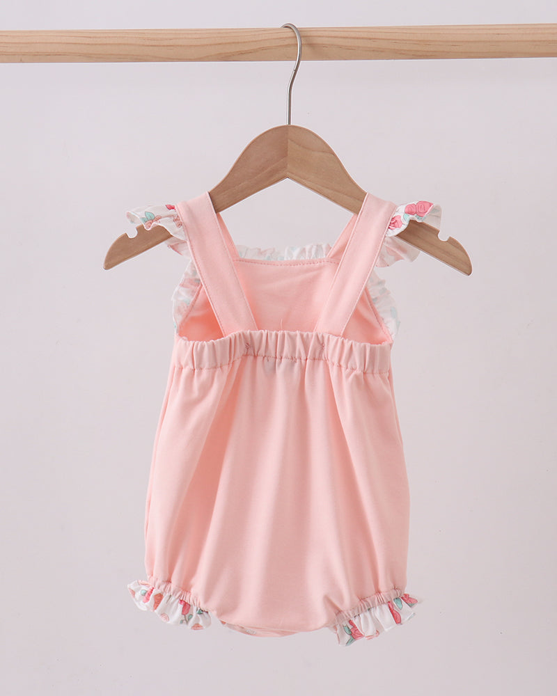 Pink baby romper with ruffled details on a wooden hanger against a light gray background