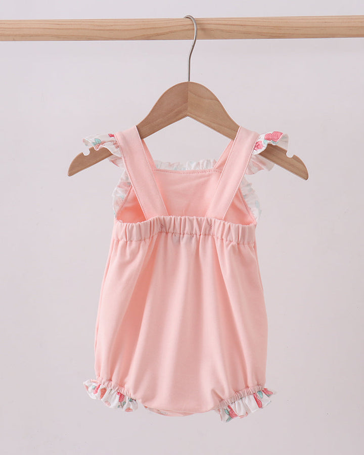 Pink baby romper with ruffled details on a wooden hanger against a light gray background