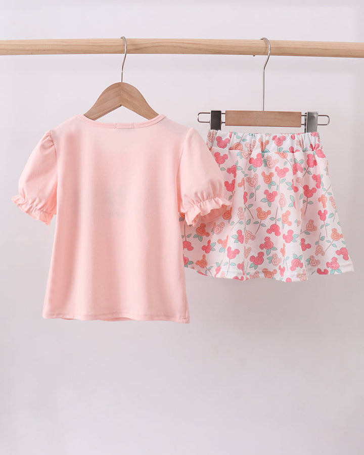 Pink top and floral skort set hanging on a wooden rod against a white background