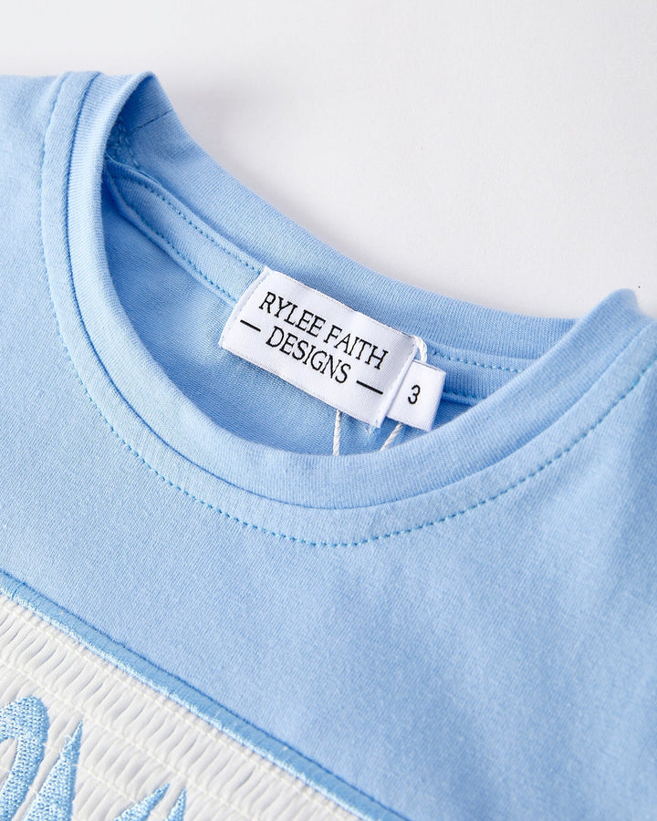 Close-up of a blue garment with a label from Rylee Faith Designs on a white background