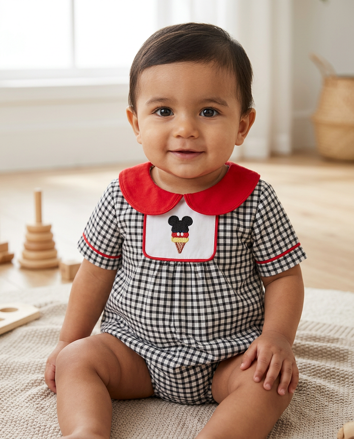 Baby wearing a checkered outfit with a red collar and ice cream design, sitting on a rug.