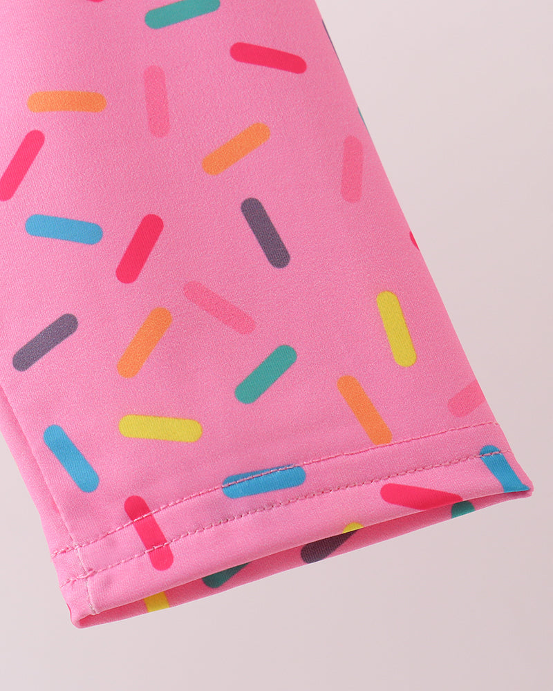Close-up of pink rashguard with colorful candy sprinkles pattern on a light gray background