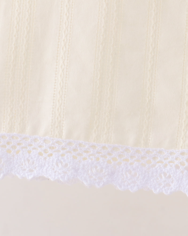 Close-up detail of a cream-colored fabric with vertical textured stripes and a white floral lace trim along the bottom edge.