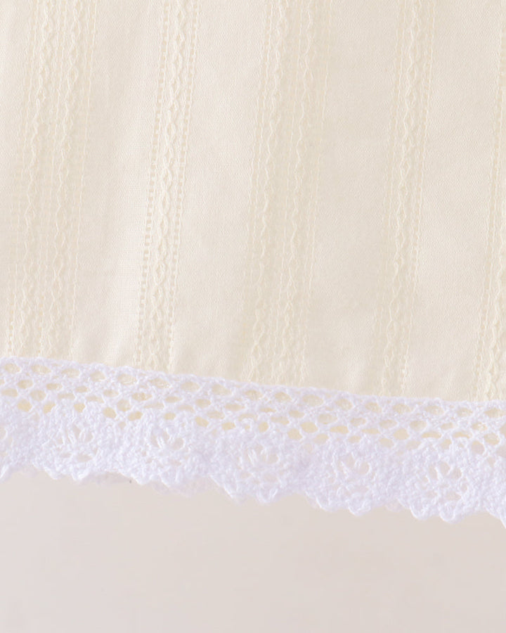 Close-up detail of a cream-colored fabric with vertical textured stripes and a white floral lace trim along the bottom edge.