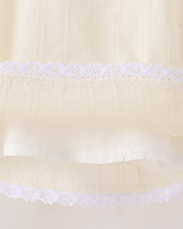 Close-up of a cream-colored fabric garment with white lace trim and vertical embroidered details.
