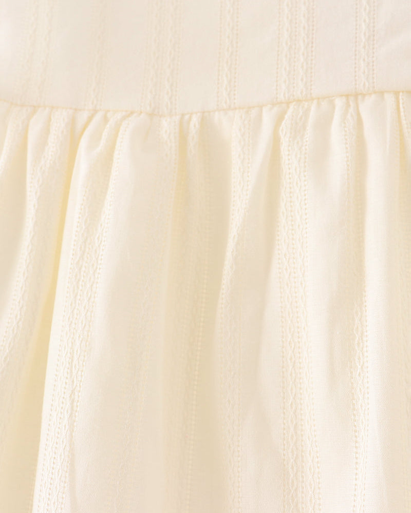 Close-up of a light cream or pale yellow dress fabric with vertical eyelet embroidery and a white lace trim at the neckline.