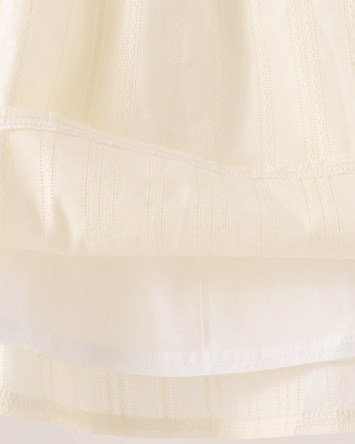 Close-up of a cream-colored fabric garment showing a tiered skirt or dress construction with embroidered vertical stripes and a sheer overlay.