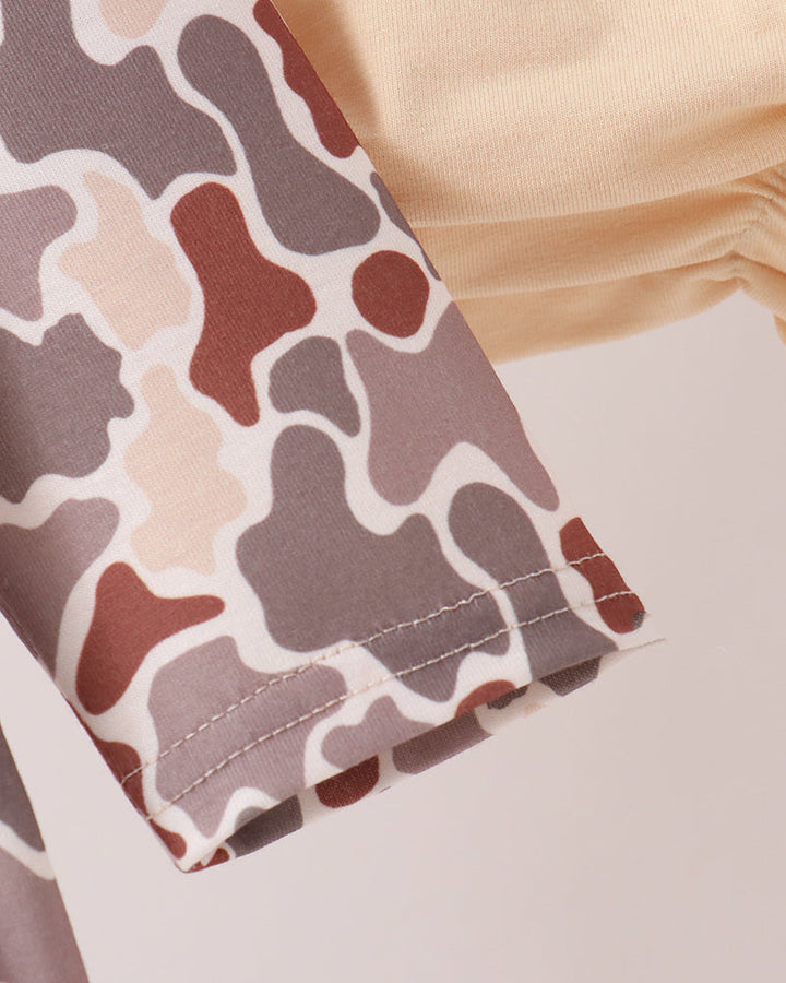 Close-up of a garment sleeve with an abstract camouflage-like pattern in taupe, brown, cream, and muted red, shown against a soft beige background.