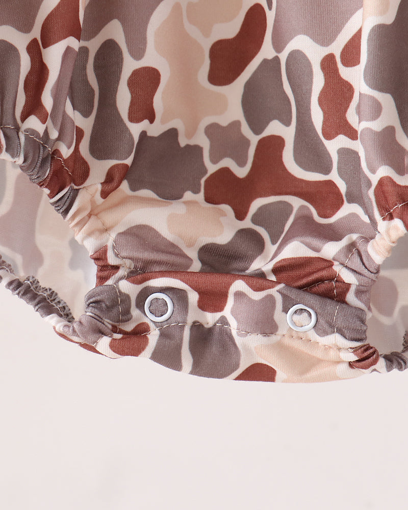 Close-up of a camouflage-patterned baby romper or diaper cover with two metal snap buttons at the crotch, shown against a plain light background.