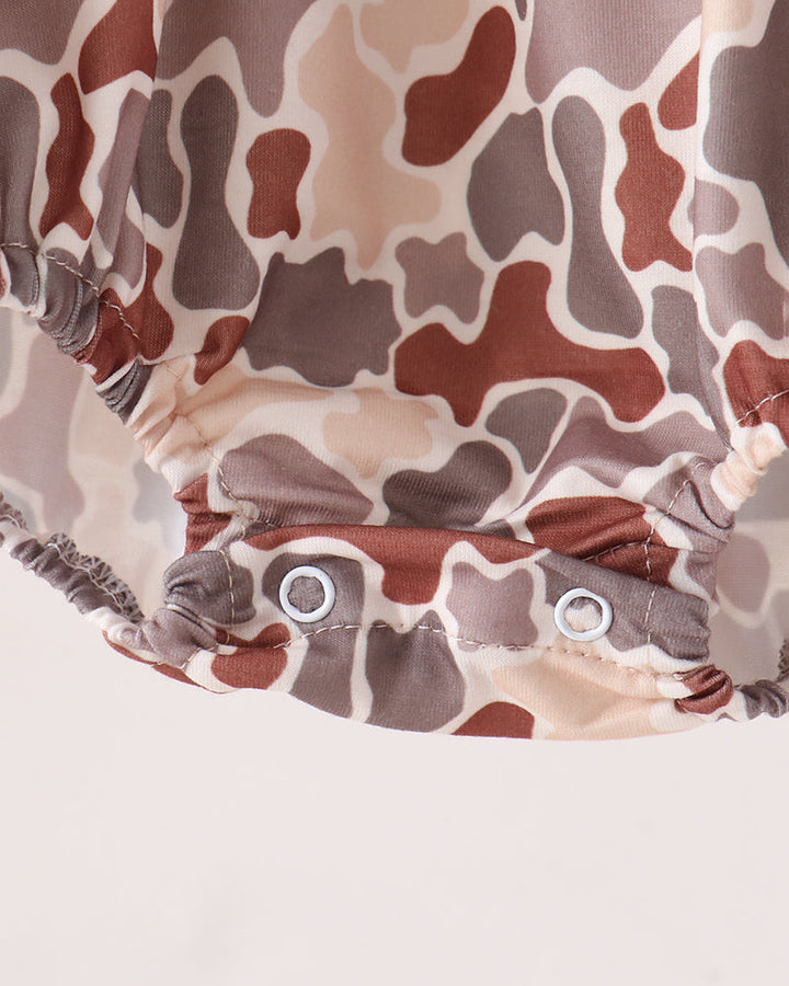 Close-up of a camouflage-patterned baby romper or diaper cover with two metal snap buttons at the crotch, shown against a plain light background.
