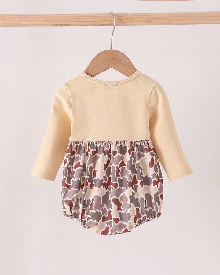 A baby long-sleeve romper hanging on a wooden hanger against a plain light background. The top is a solid pale cream color, and the gathered bottom features a brown, gray, and beige camouflage pattern.