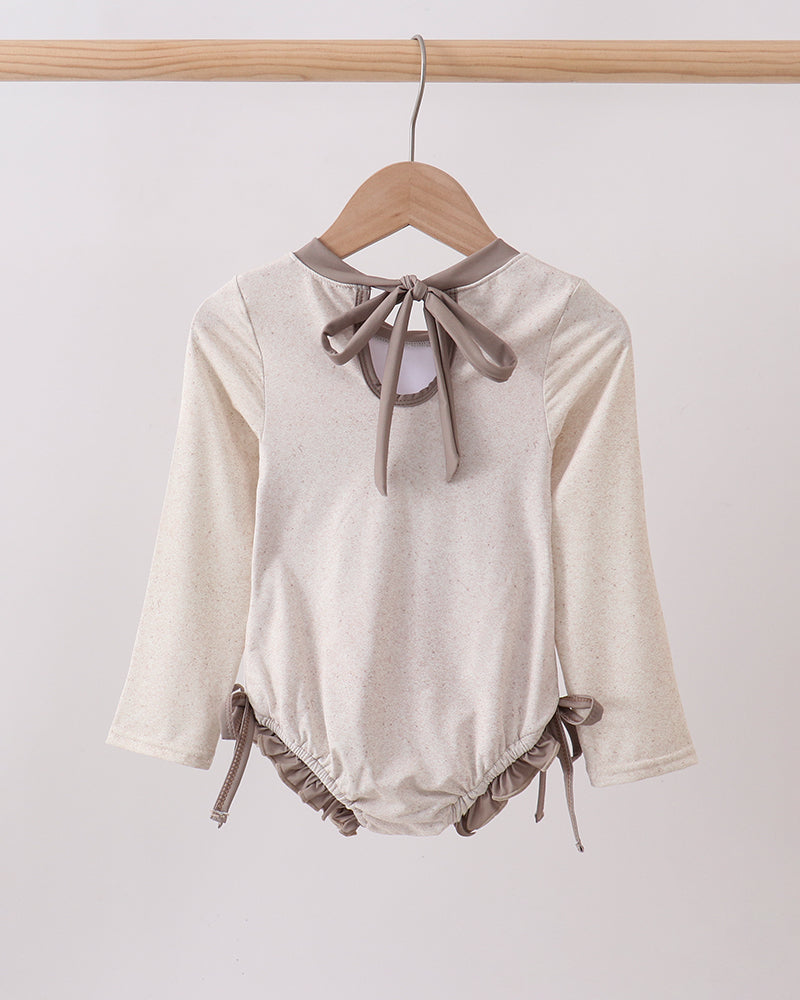 Rashguard with long sleeves and bow details on a hanger against a white background