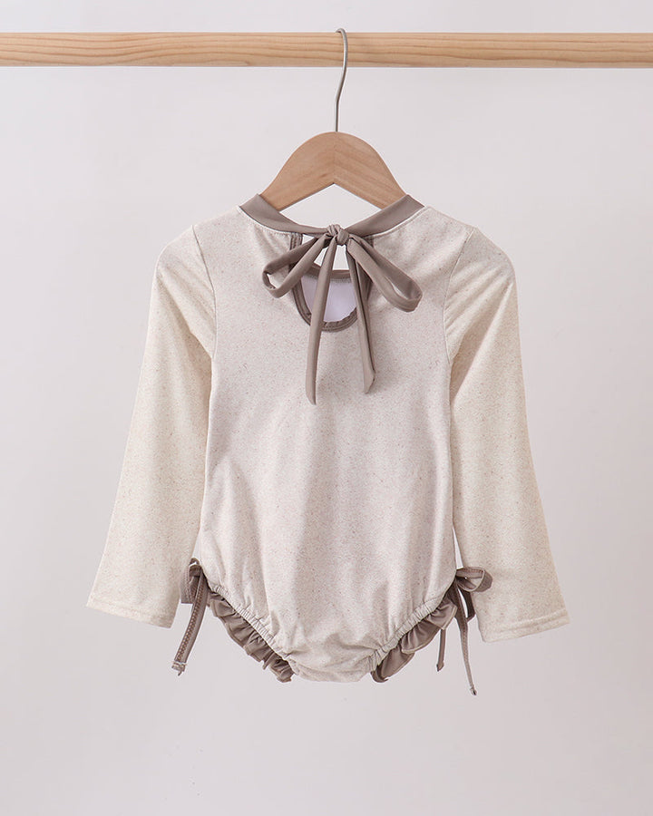 Rashguard with long sleeves and bow details on a hanger against a white background