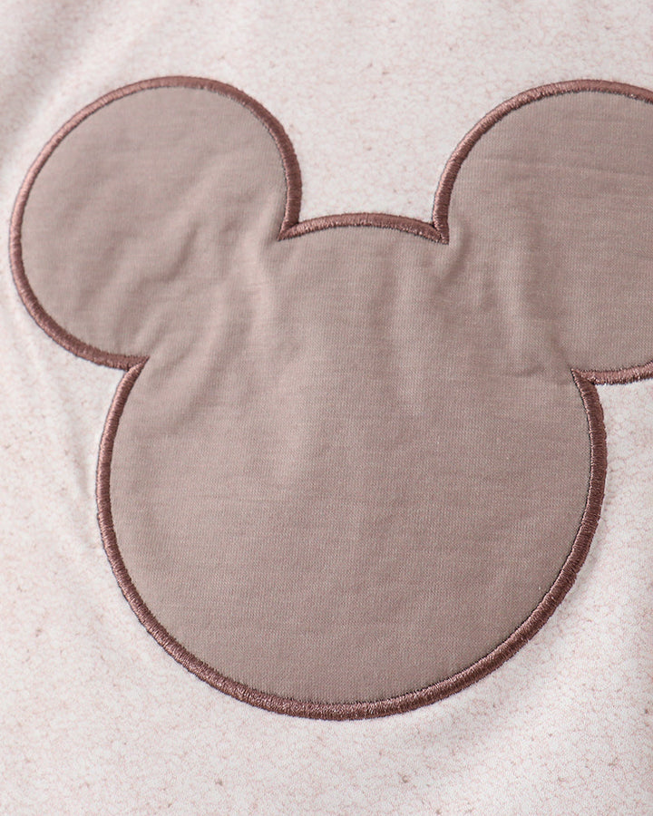 Close-up of a textured fabric with a large, rounded, beige mouse ear design.