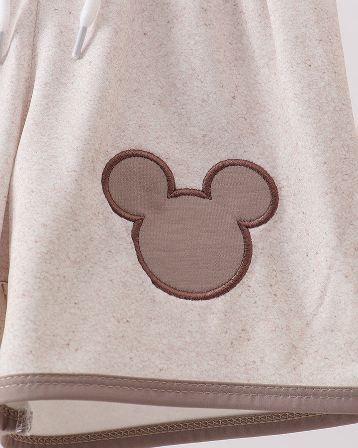 Close-up of a beige swim trunks with a brown embroidered design on a white background