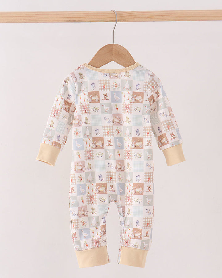 A baby long-sleeve footless jumpsuit with an all-over patchwork animal print, hanging on a wooden hanger from a light wood rod against a plain off-white background.