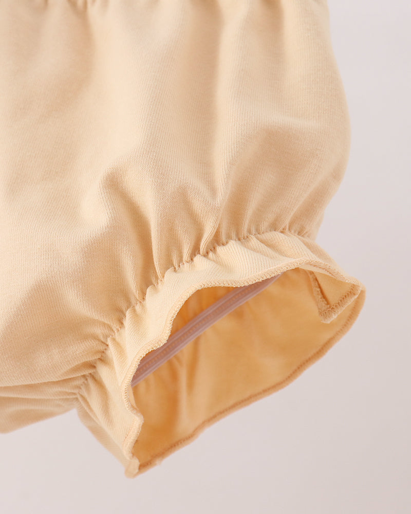 Close-up detail of a light beige fabric garment, showing gathered elastic trim and a smooth inner lining on a plain light background.