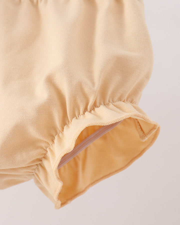 Close-up detail of a light beige fabric garment, showing gathered elastic trim and a smooth inner lining on a plain light background.