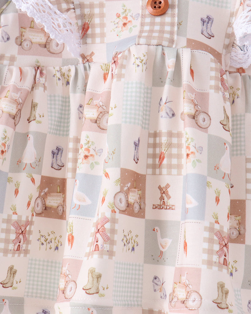 A close-up of a patchwork-patterned dress or fabric garment featuring pastel squares with small illustrations of farm animals, bicycles, carrots, flowers, and gingham checks in soft pink, beige, blue, and cream tones.