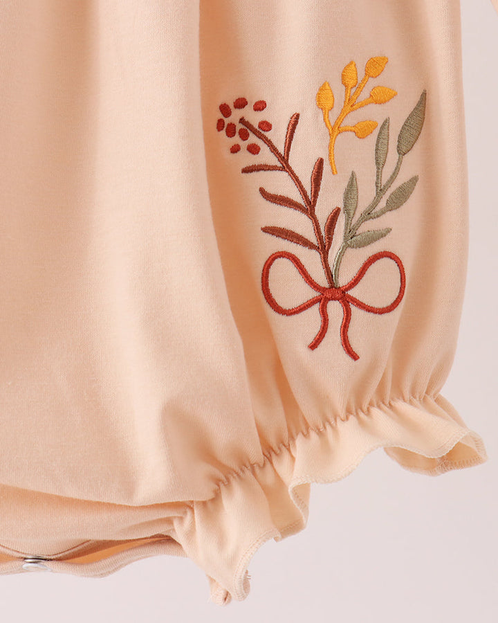Beige bubble romper with floral embroidery on front and gathered sleeve cuffs