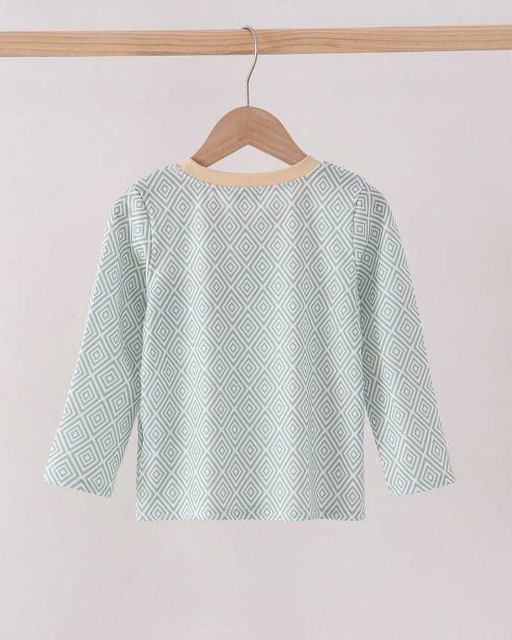 A long-sleeve boys top with a light mint green and white geometric diamond pattern, hanging on a wooden hanger from a wooden clothes rack against a plain light beige background.