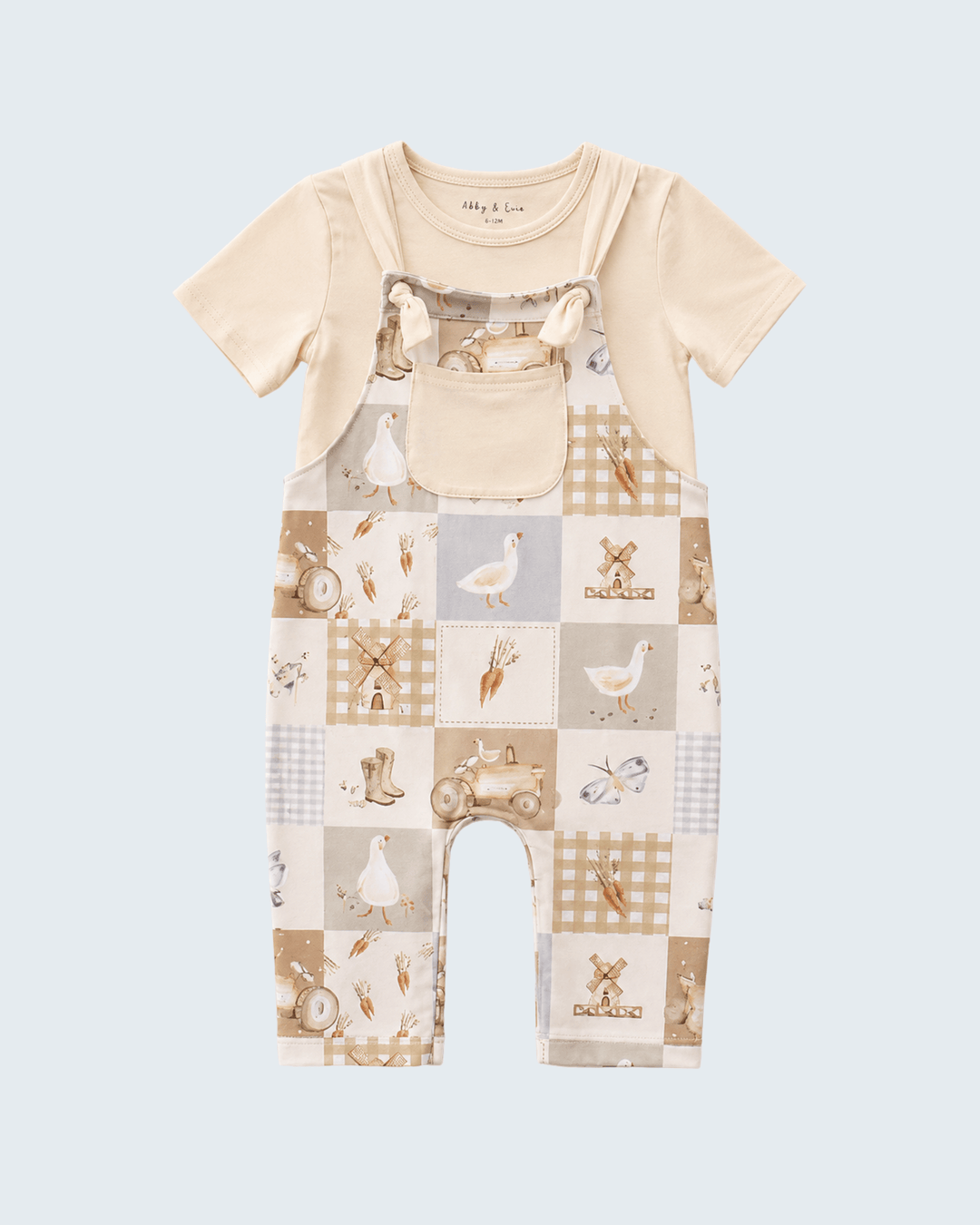 A baby short-sleeve romper in a cream and beige patchwork print featuring gingham, stripes, and illustrations of farm animals and vehicles, shown against a light blue-gray background.