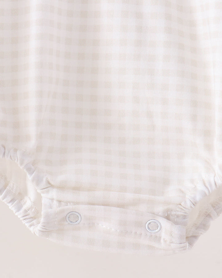 Close-up of a baby romper or bodysuit bottom corner with a soft cream and beige gingham check pattern and snap closures.