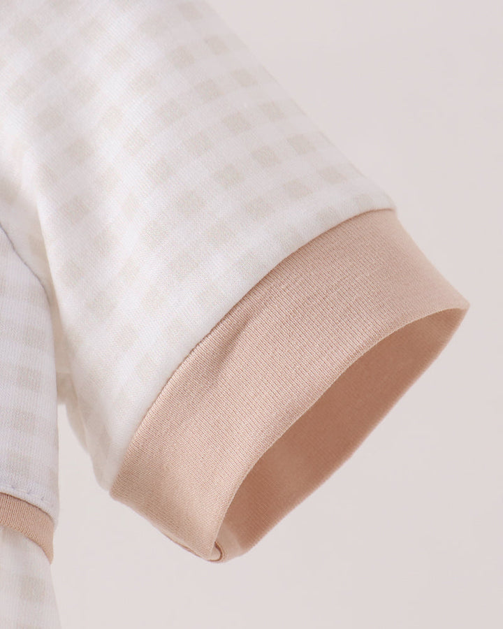 Close-up of a sleeve with a white and beige gingham pattern and a solid beige ribbed cuff, shown against a light beige background.