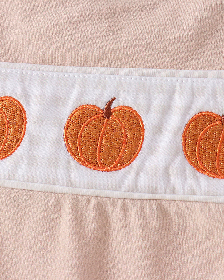 Close-up of a peach-colored garment with a white horizontal band featuring embroidered orange pumpkins.