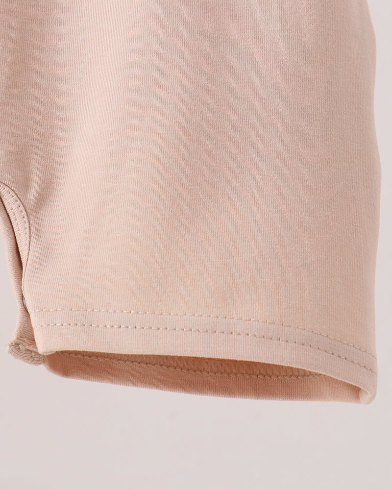 Close-up of a light beige or pale peach knit fabric, showing the texture and hem stitching detail against a plain light background.