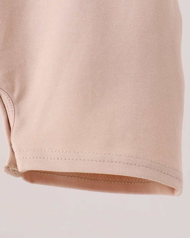 Close-up of a light beige or pale peach knit fabric, showing the texture and hem stitching detail against a plain light background.