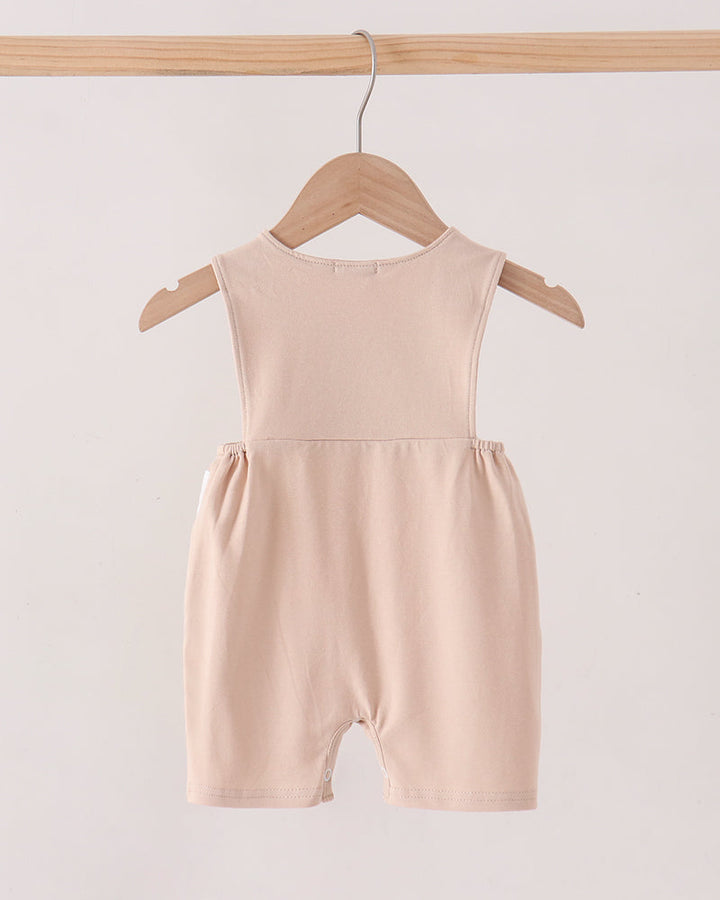 A sleeveless baby romper in a soft blush pink color, hanging on a wooden hanger from a wooden clothing rack against a plain off-white background.