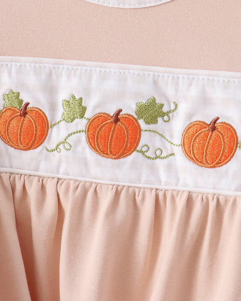 Close-up of a peach-colored dress with a white horizontal band featuring embroidered orange pumpkins and green leaves.