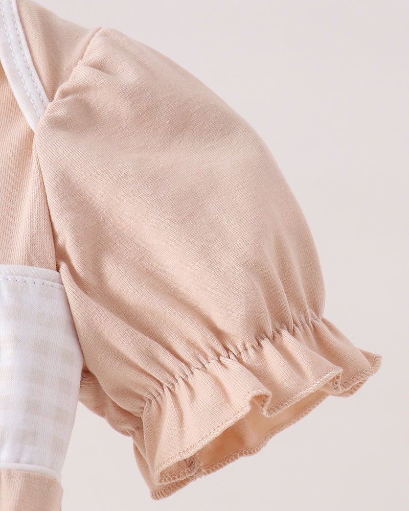 Close-up of a baby top featuring a soft peach-beige puff sleeve with a ruffled hem and a white gingham check pocket.