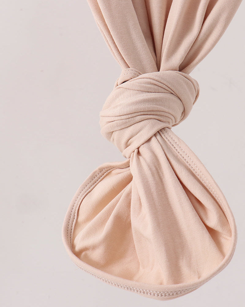 A close-up of a soft blush pink fabric accessory, likely a small pouch or pouch-like textile item, tied in a knot at the top and shown against a plain light background.