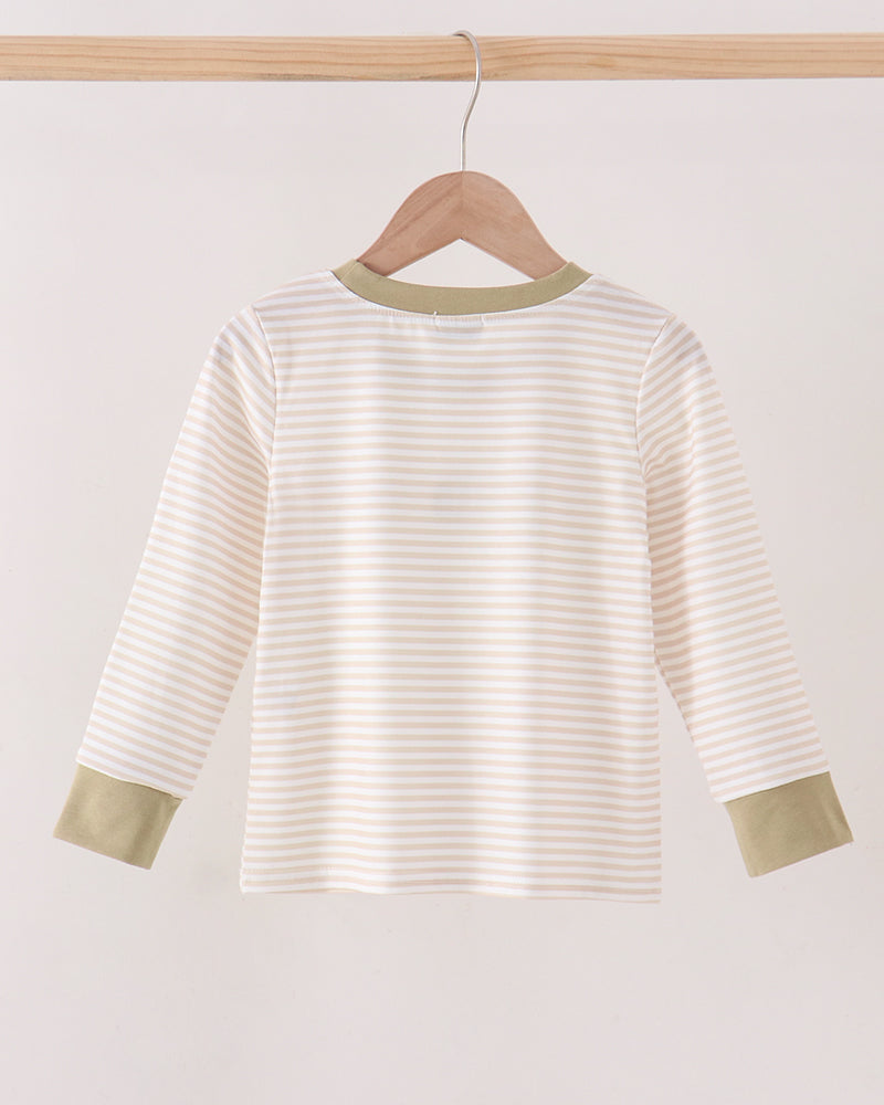 A long-sleeve top with thin beige and white horizontal stripes, featuring solid sage green trim at the crew neck and cuffs, hanging on a wooden hanger from a light wood bar.