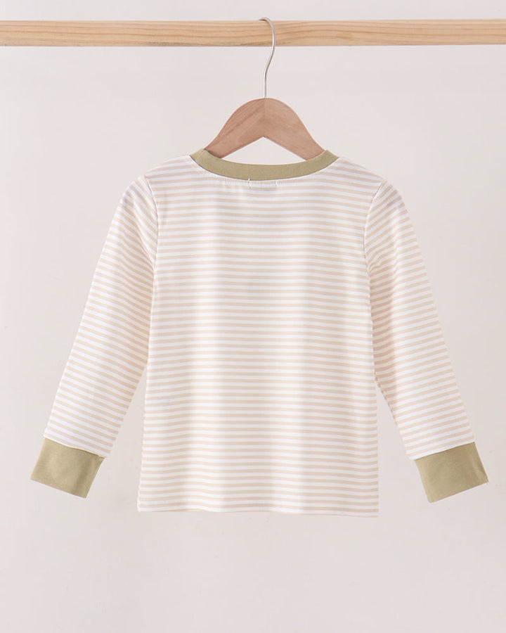 A long-sleeve top with thin beige and white horizontal stripes, featuring solid sage green trim at the crew neck and cuffs, hanging on a wooden hanger from a light wood bar.