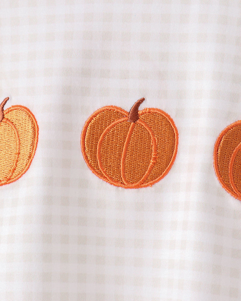Close-up of a white gingham fabric garment featuring orange embroidered pumpkins on the front.