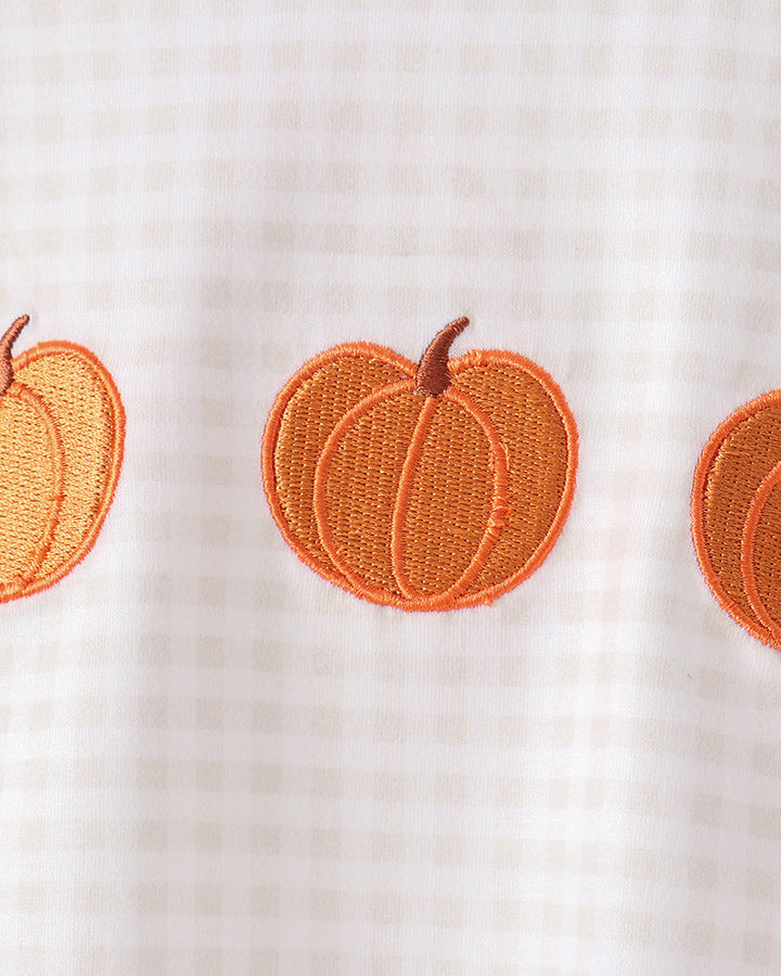 Close-up of a white gingham fabric garment featuring orange embroidered pumpkins on the front.