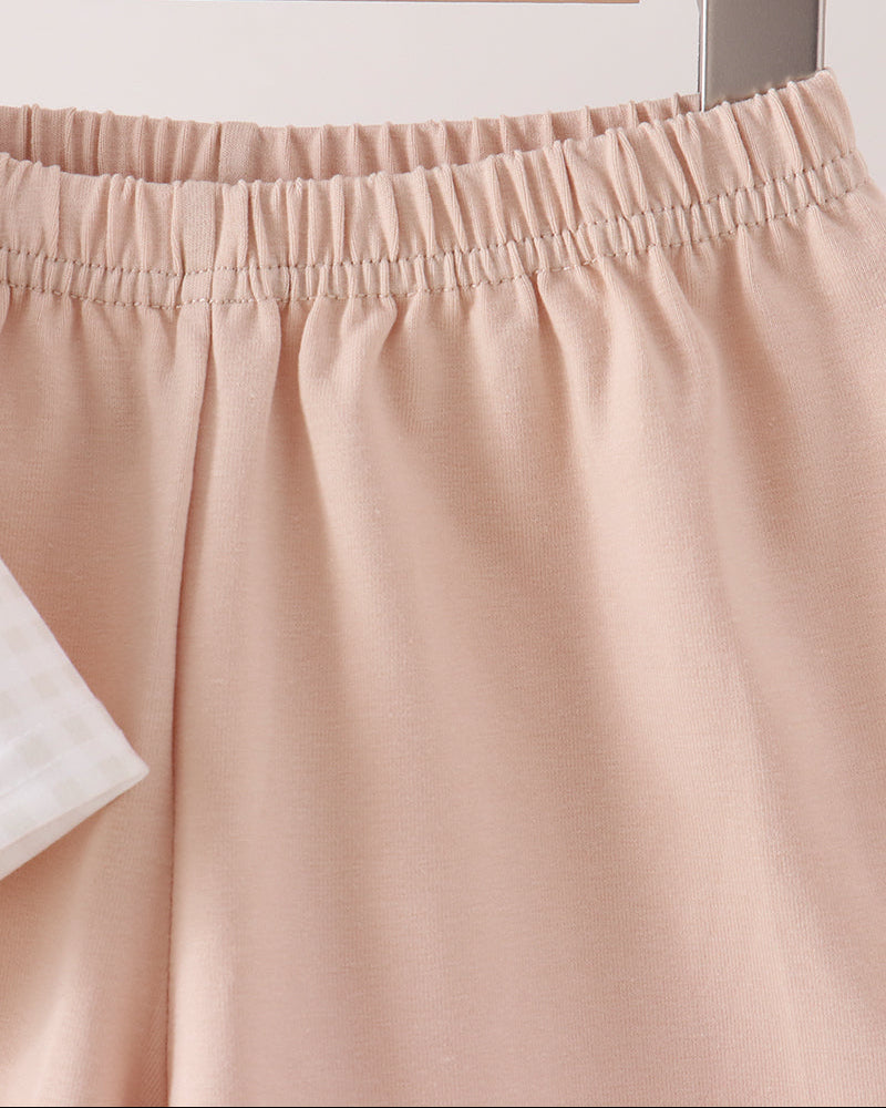 Close-up of a beige shorts with an elastic waistband, hanging on a wooden hanger against a light neutral background.