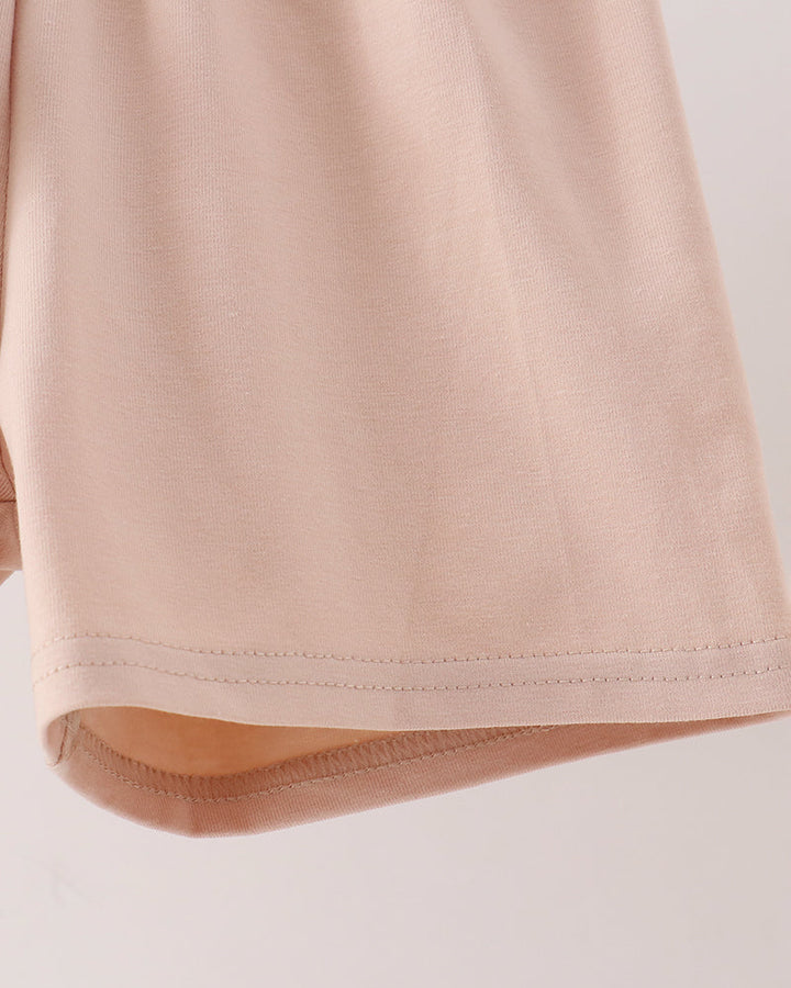 Close-up of a light beige colored garment, showing the hem and fine stitching detail against a plain light background.